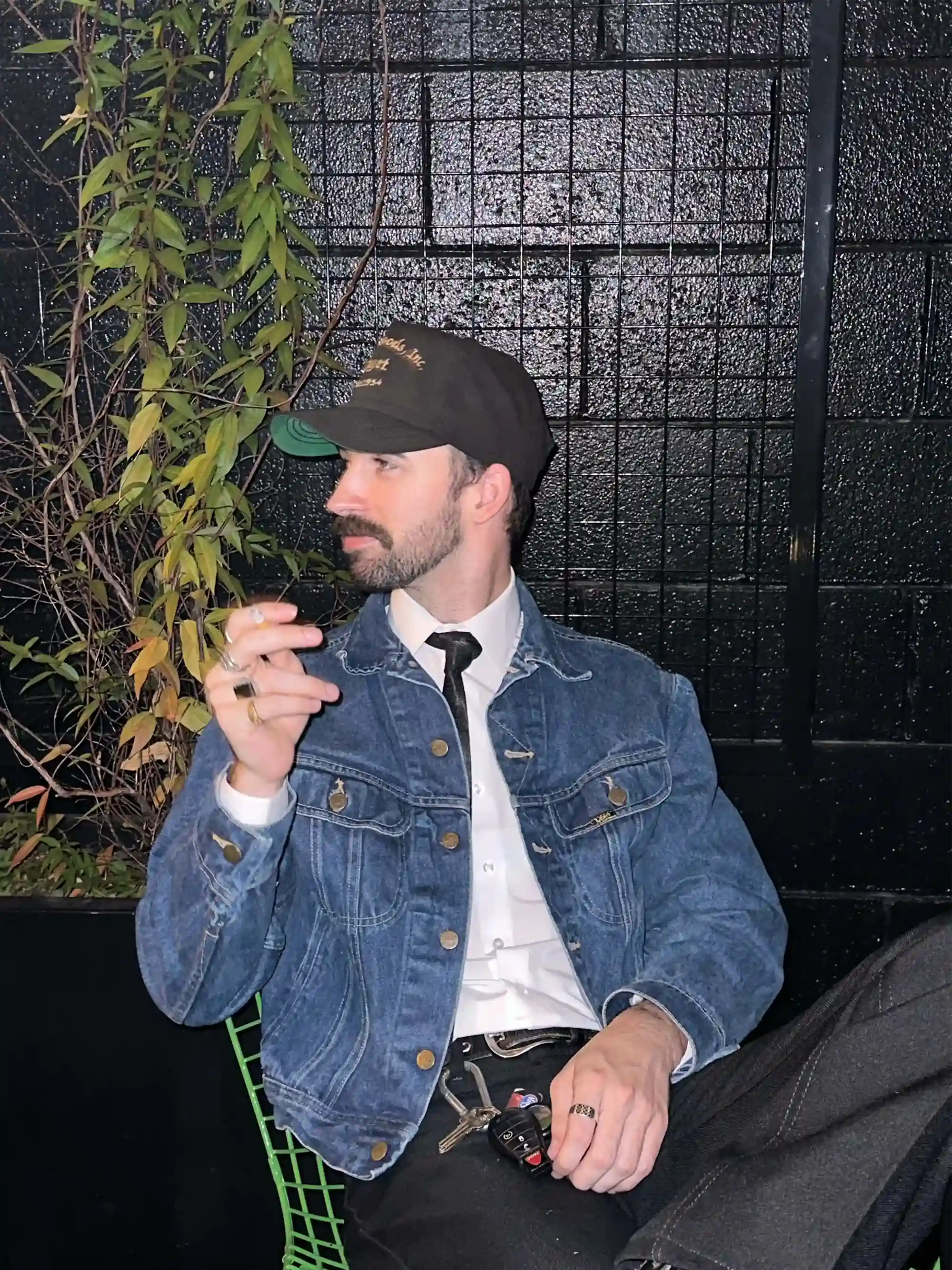 Find this outfit: Man smoking a cigarette in a denim coat, black ball cap, and a silver ring.